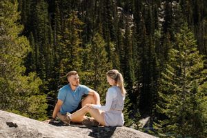 A couple reads maps while sitting on a rocky mountain ledge surrounded by dense evergreen forest. Colchuck Lake proposal