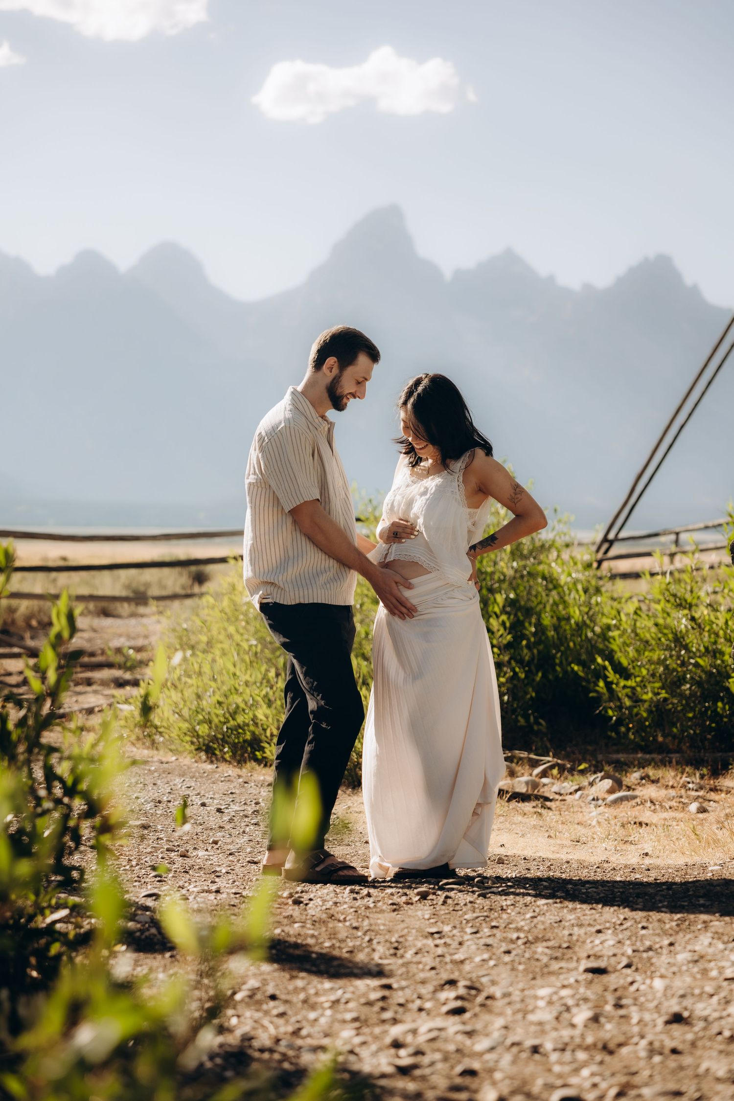 Romantic couple embraces in a spiraling dance move on a mountain road with the Grand Tetons peaks in the background.