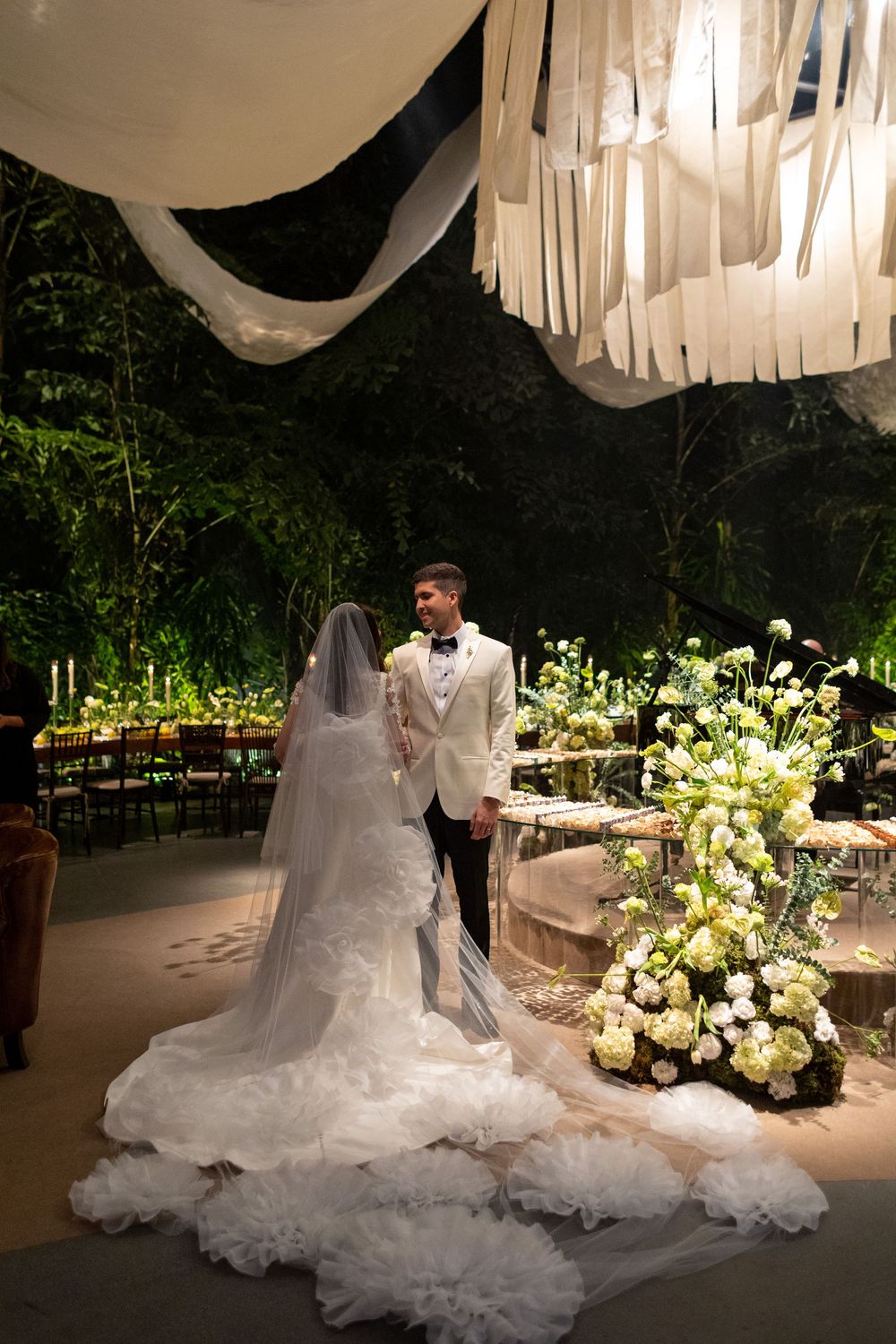 Elegant wedding reception at night with white drapery decorations and illuminated floral arrangements creating a romantic atmosphere.