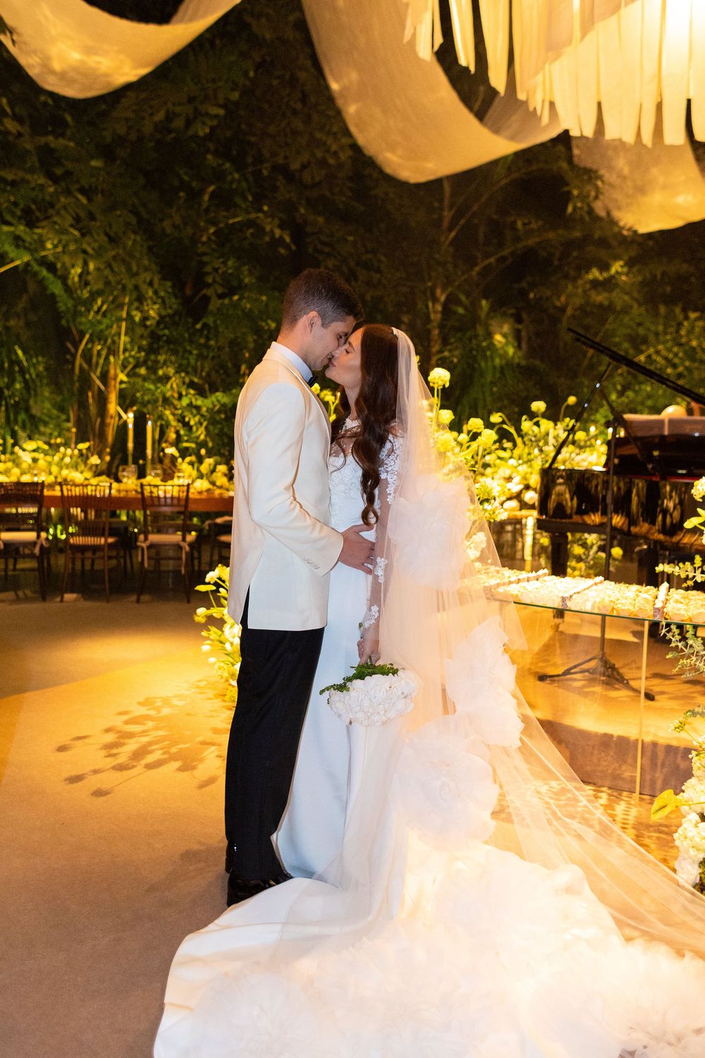 Couple dancing at an outdoor evening wedding reception beneath white fabric draping and warm lighting.