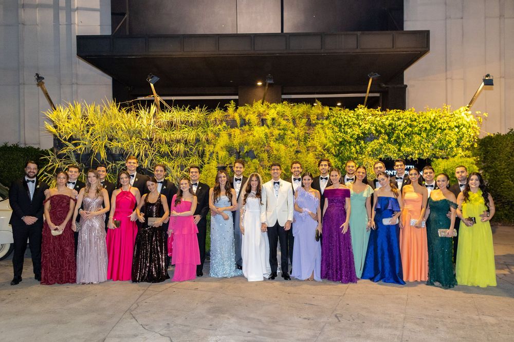 Wedding party lineup featuring bridesmaids in colorful dresses ranging from pink to yellow to blue standing outdoors.