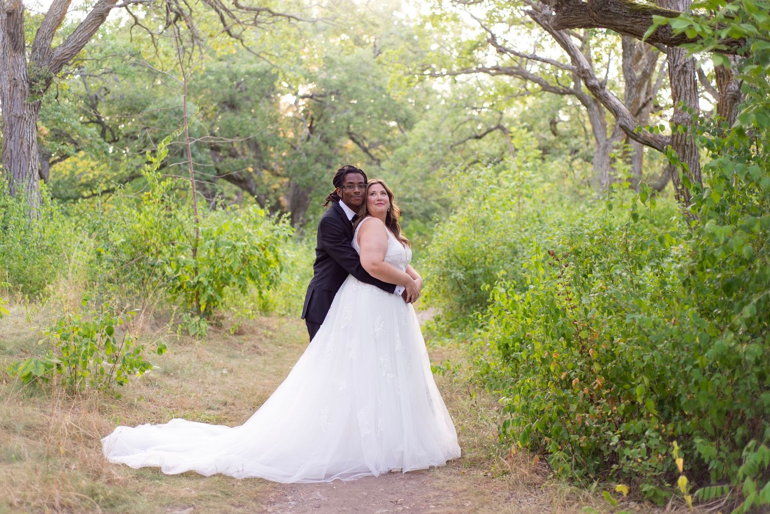 A couple in a romantic wedding portrait series set in a lush garden pathway with natural greenery and sunlight.
