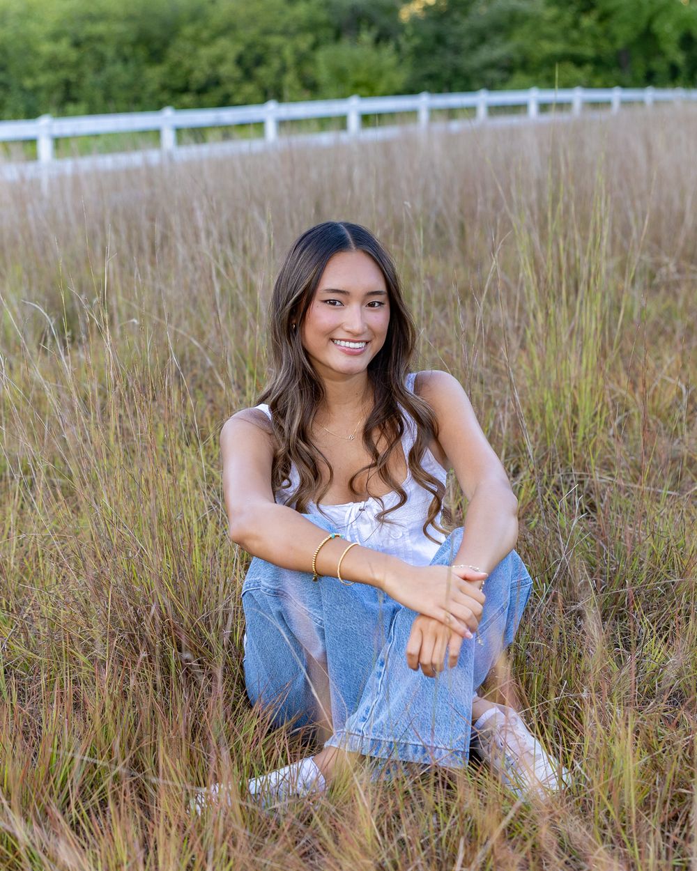 A high school senior poses for her yearbook portraits in a grassy field at  Wolbach Farm in Sudbury, MA with Lisa West Photography.
