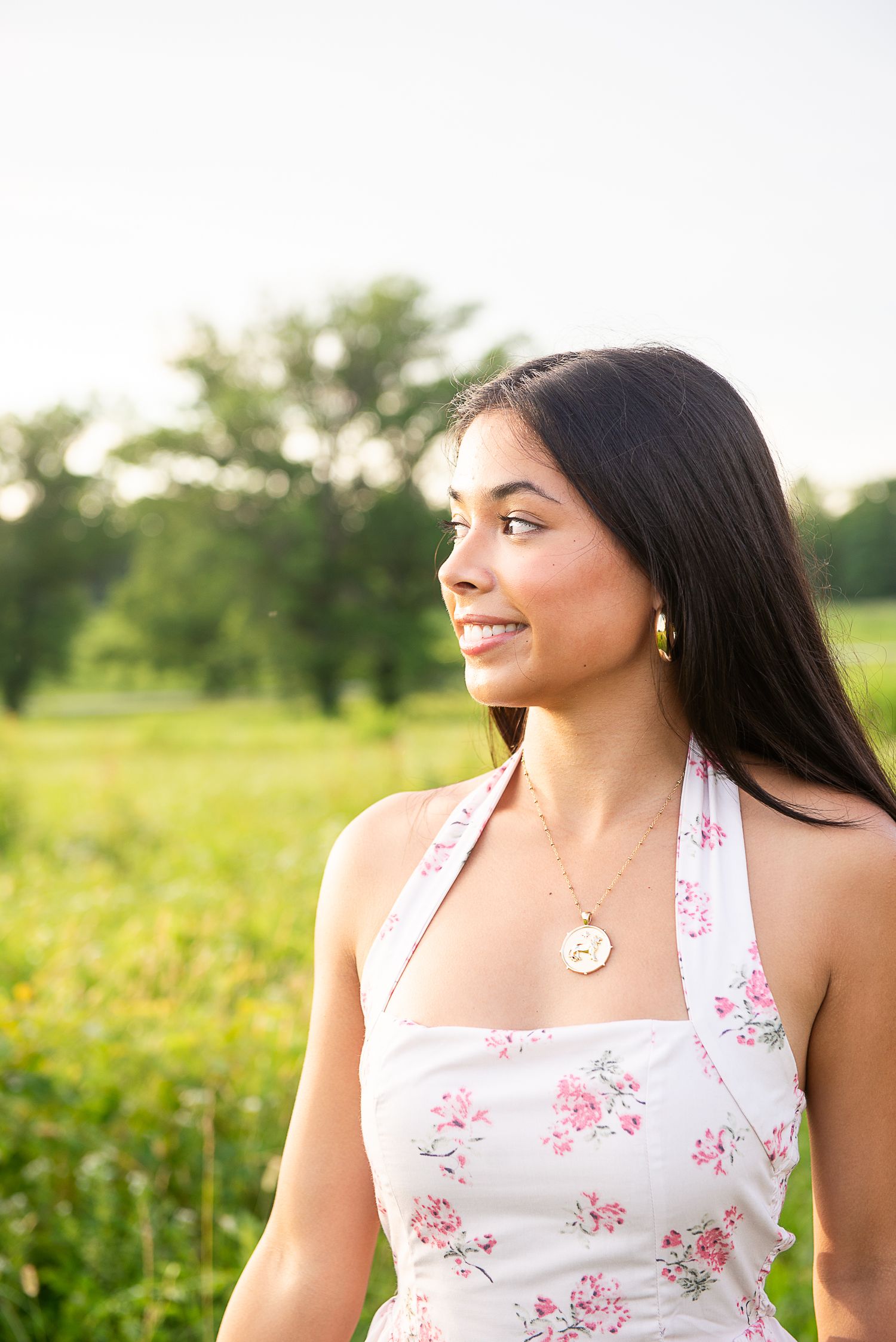 Smiling person in a white floral top poses in a sunny field during golden hour.