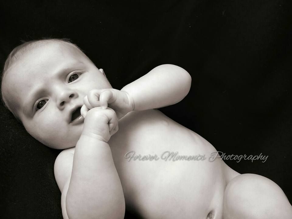 Black and white series of artistic photographs capturing a newborn baby in soft, natural poses on dark backdrop.