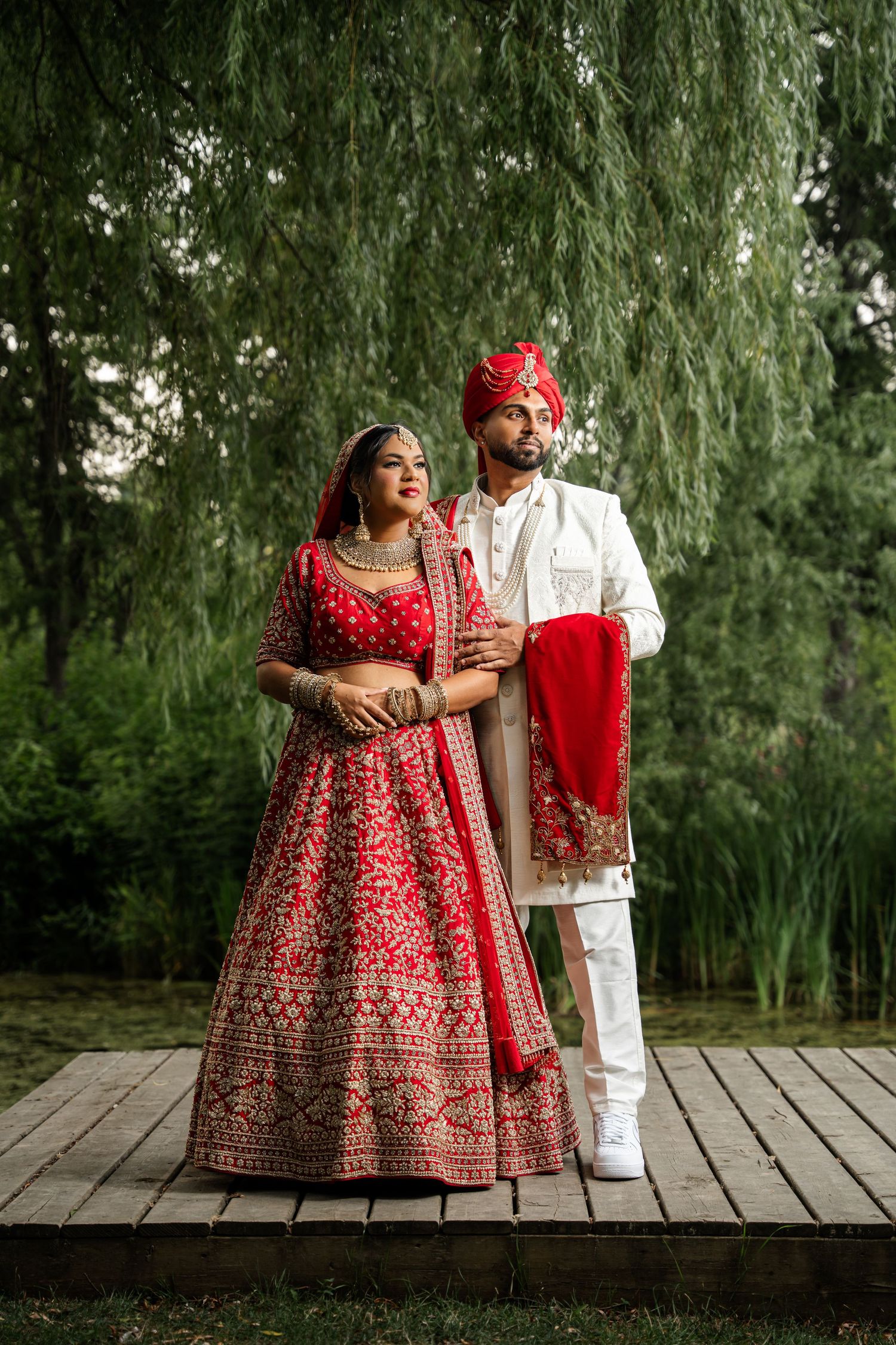 Traditional Indian wedding attire showcased under weeping willow trees with rich red lehenga details.