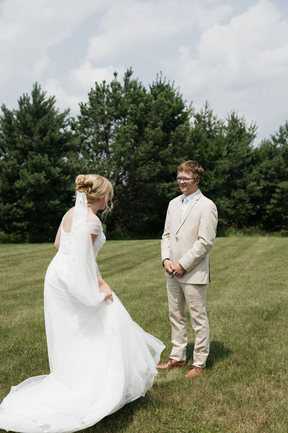 A couple shares their first look moment at an outdoor wedding ceremony with pine trees in the background.