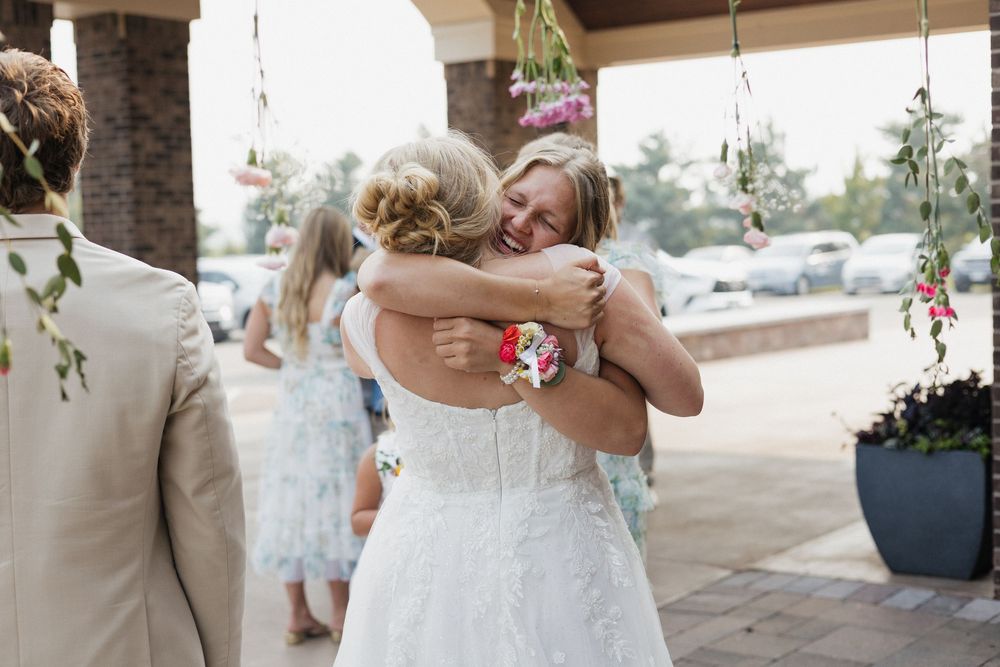 Two people embrace in an emotional moment during a wedding ceremony under a covered outdoor venue.