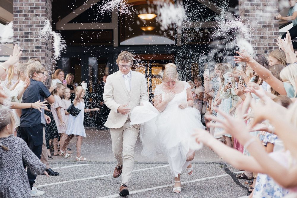 Wedding couple exits venue under a shower of floating flower petals as guests celebrate their special moment.