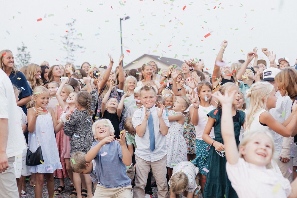 A large group of wedding guests celebrates by throwing confetti while cheering outdoors.