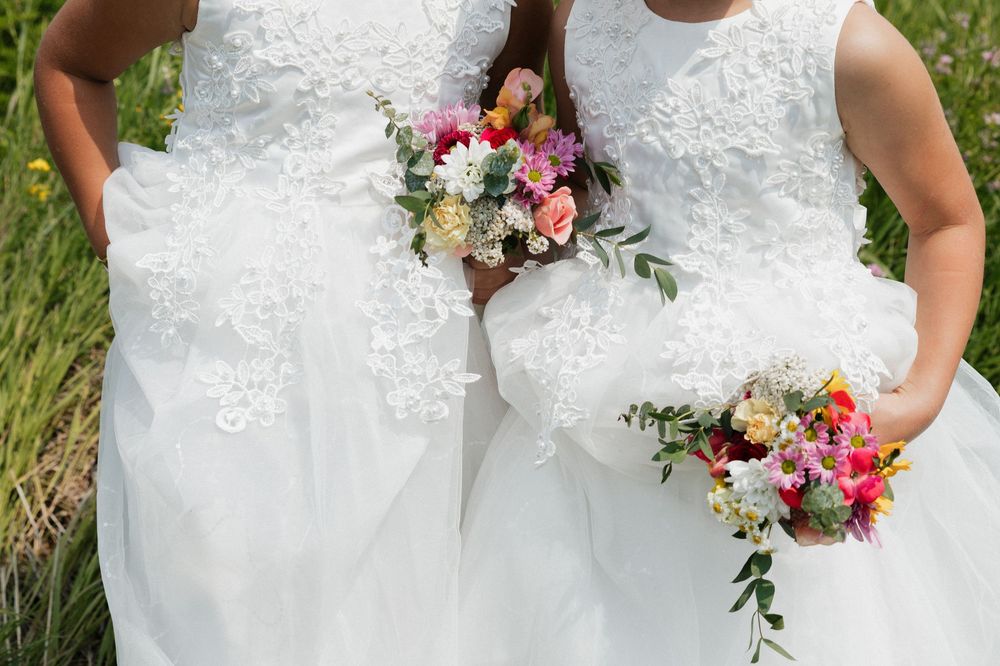 Close-up of two white lace wedding dresses with colorful floral bouquets.