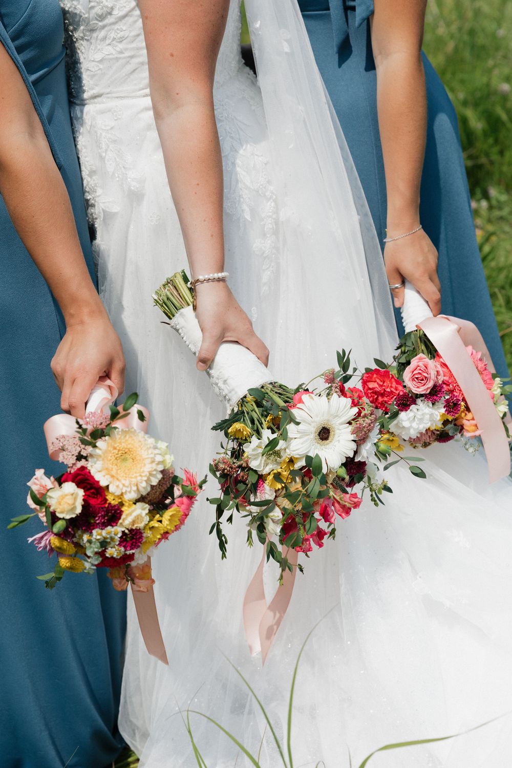 Close-up of colorful wedding bouquets held by bridesmaids in teal dresses against white dress.