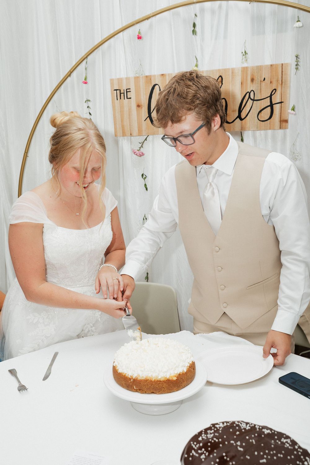 A couple cuts into their wedding cake together during their reception under a decorative arch.