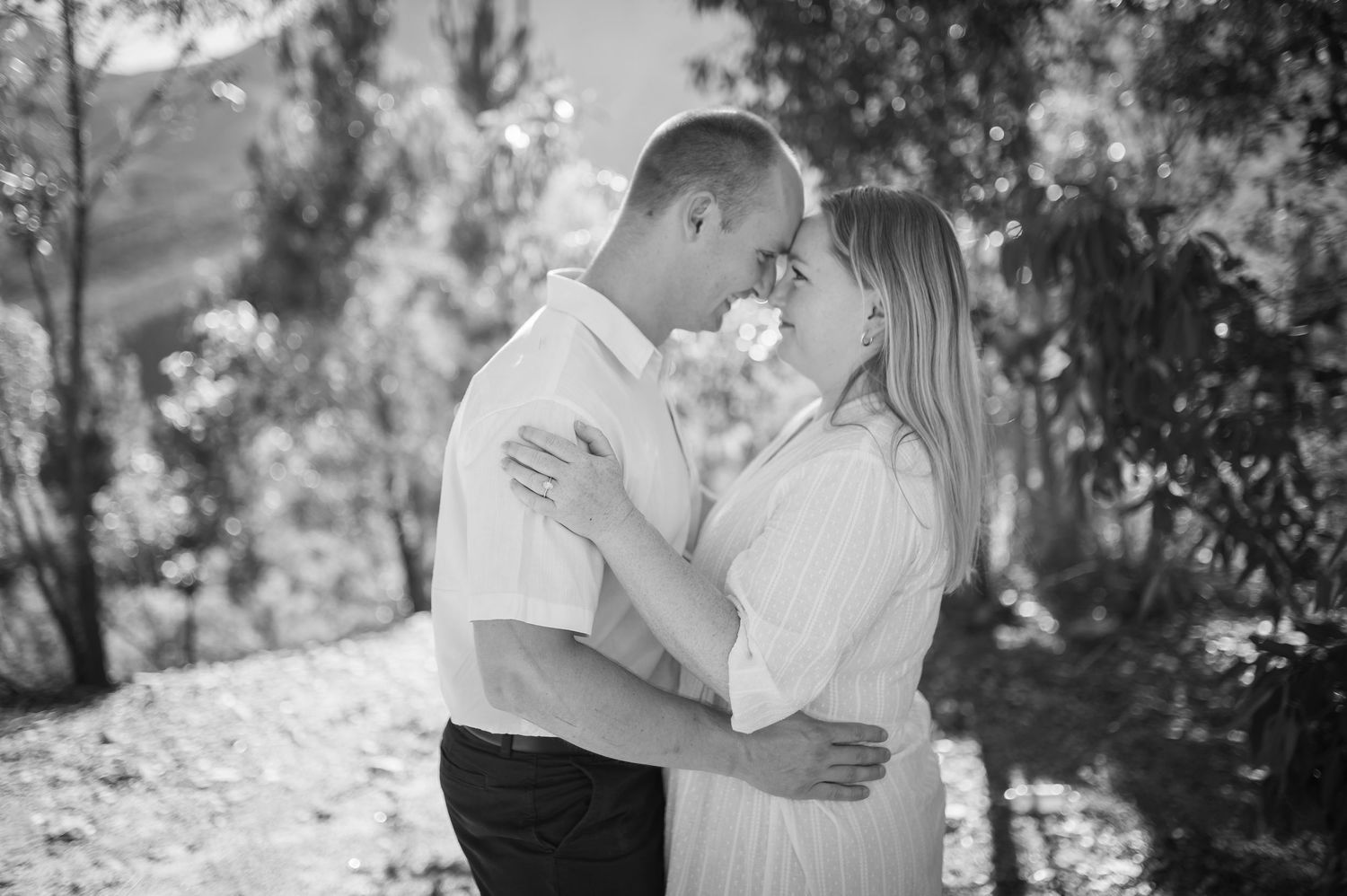 Black and white engagement photo series with romantic couples embracing outdoors among trees and natural settings.