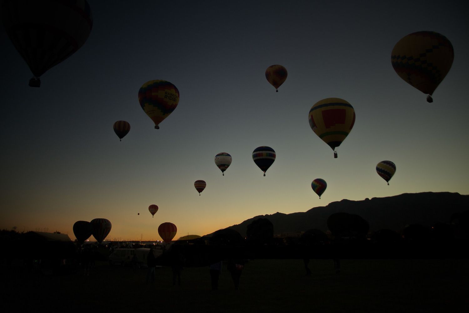Silhouettes of hot air balloons floating against a darkening sky during sunset.