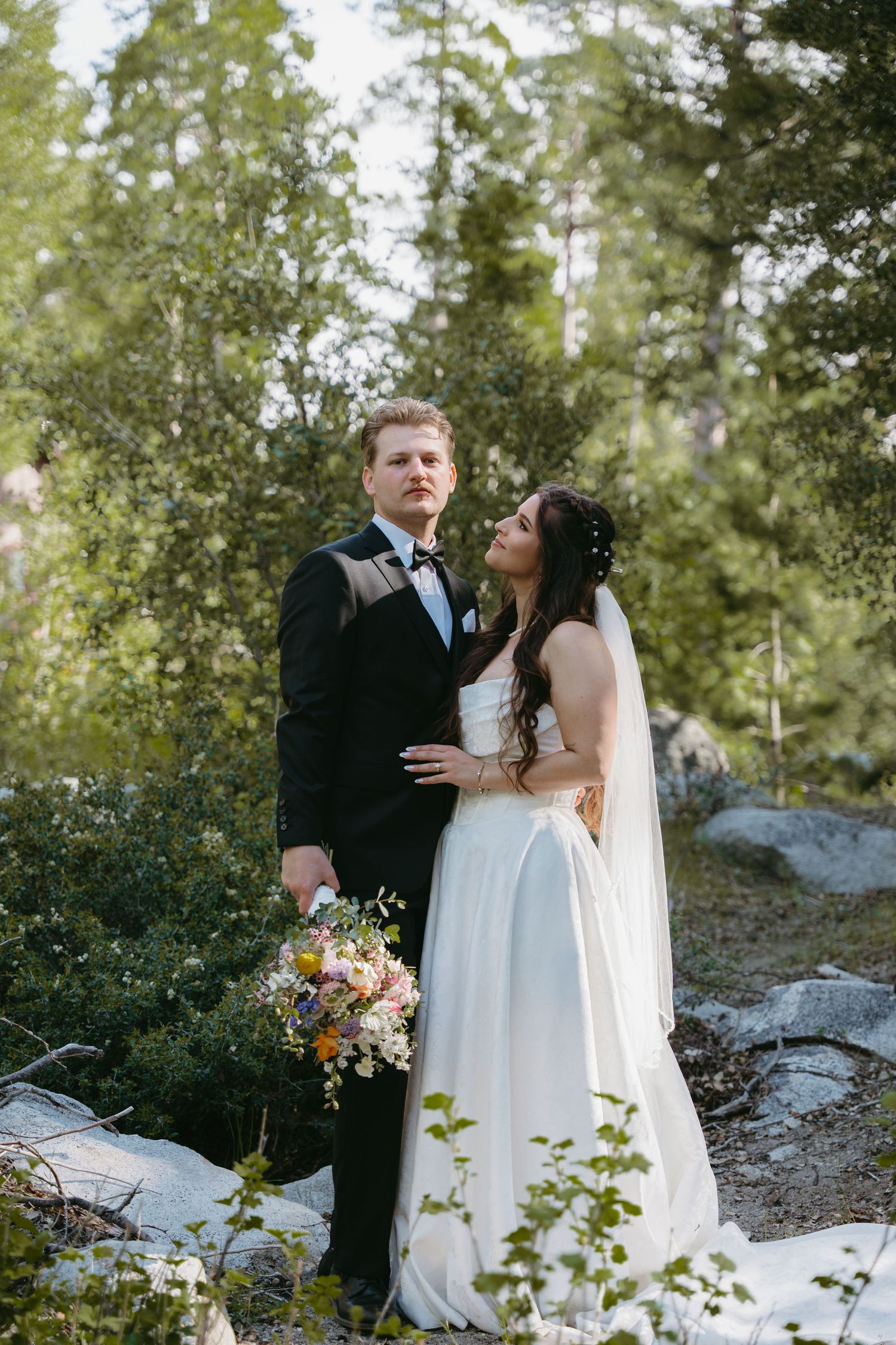A white wedding dress hangs on the porch of a charming Victorian-style house with blooming flowers.