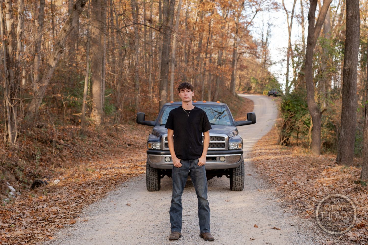 Person standing on dirt path with Dodge Ram truck and fall foliage in background.