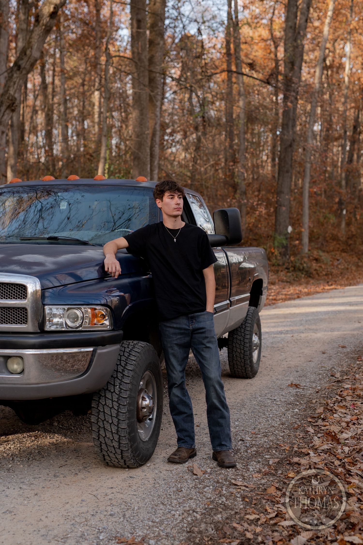 A person stands next to their lifted black Dodge Ram truck on a wooded trail.