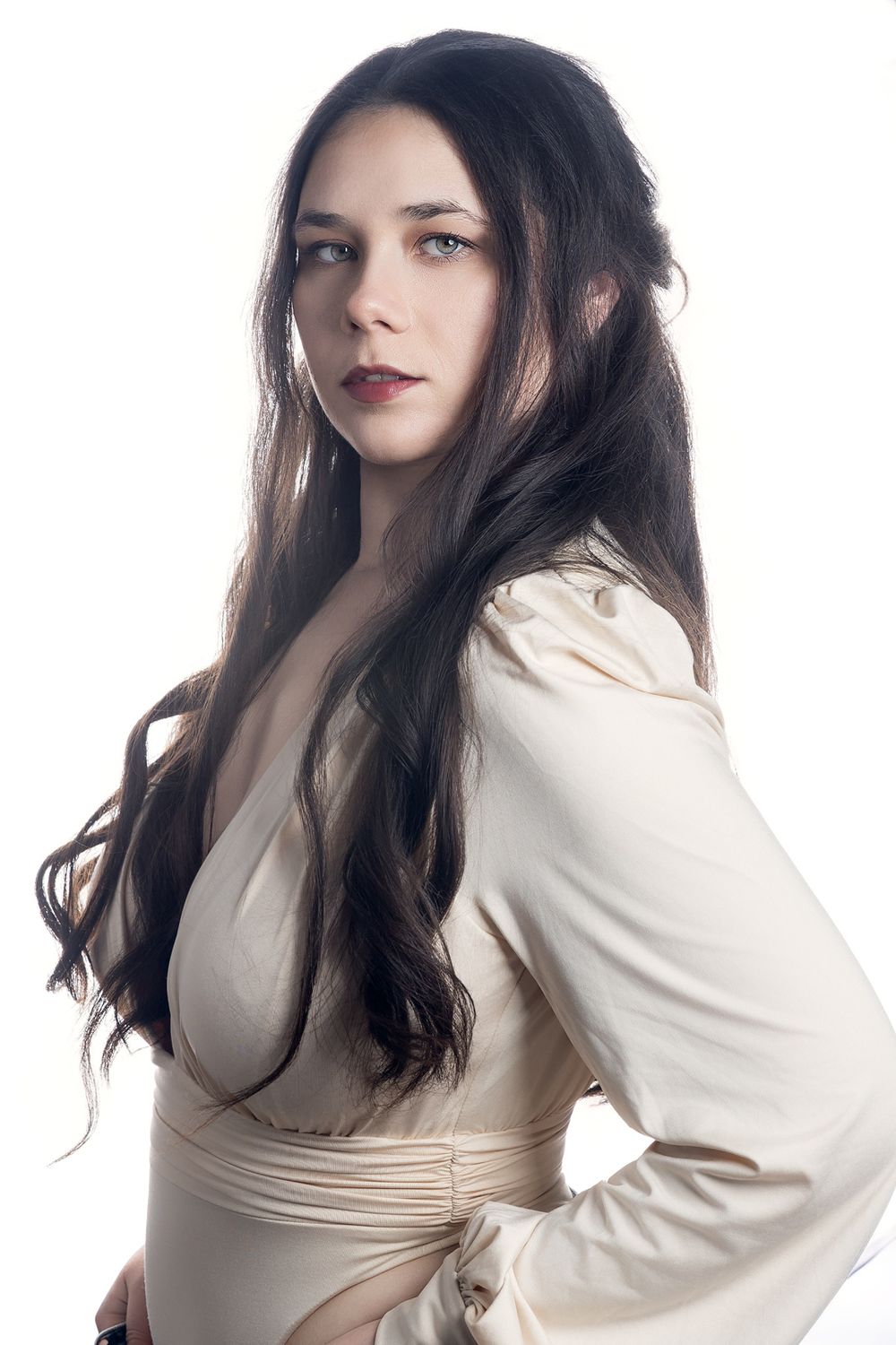 Young woman with long dark hair wearing a cream wrap dress poses against a white background.