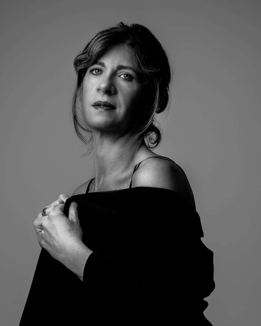 Black and white portrait of a woman in an off-shoulder top, gazing confidently at the camera.