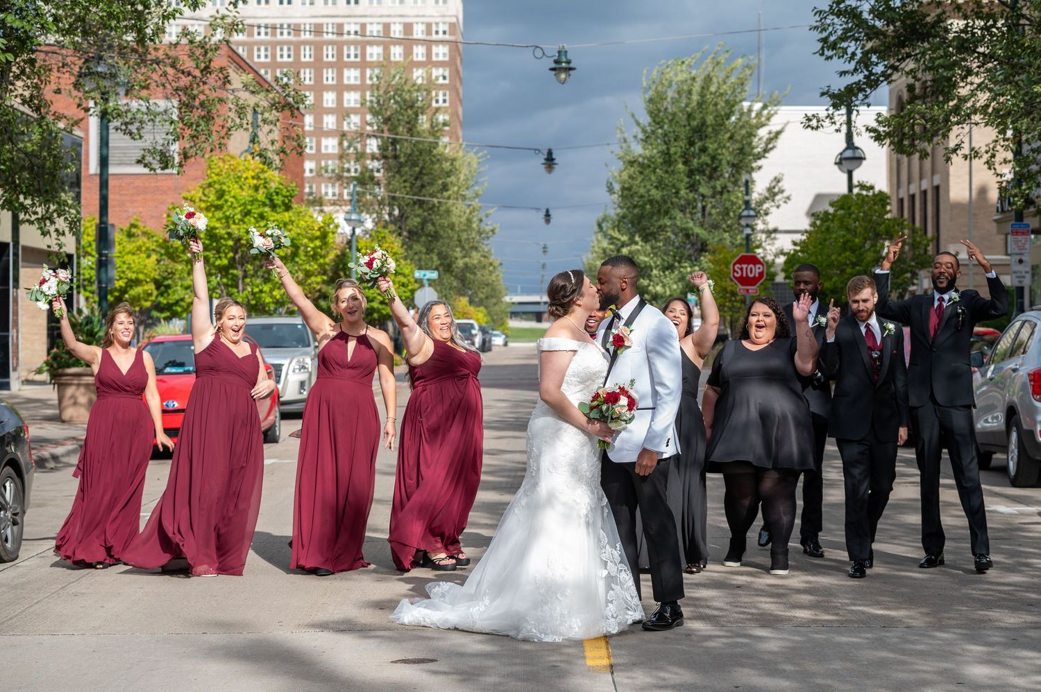 Wedding party in burgundy dresses and dark suits poses for photos on an urban street.