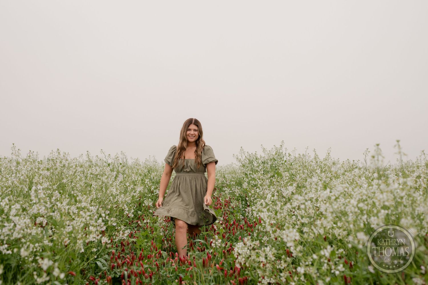 An ethereal outdoor scene with someone in a sage dress standing among white and red blooms.