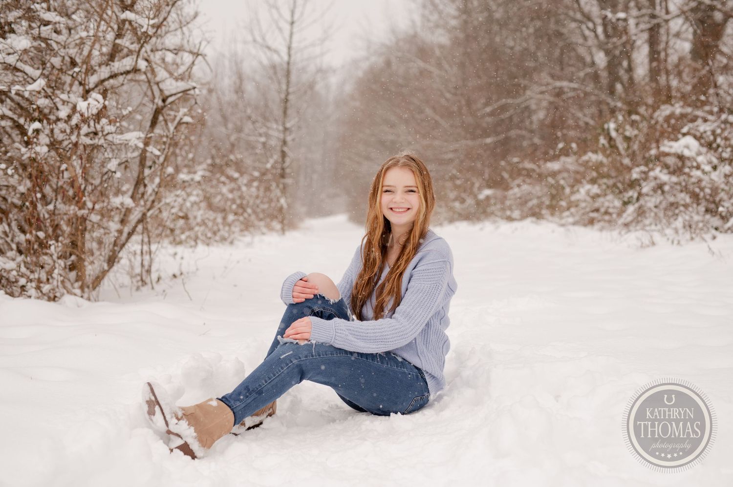 A person relaxes in snow wearing blue winter attire against a snowy forest backdrop.