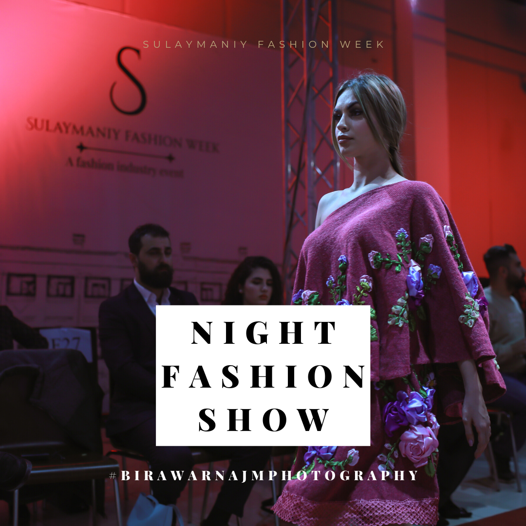 A model walks the runway wearing a pink embroidered dress at a night fashion show with dramatic red lighting.
