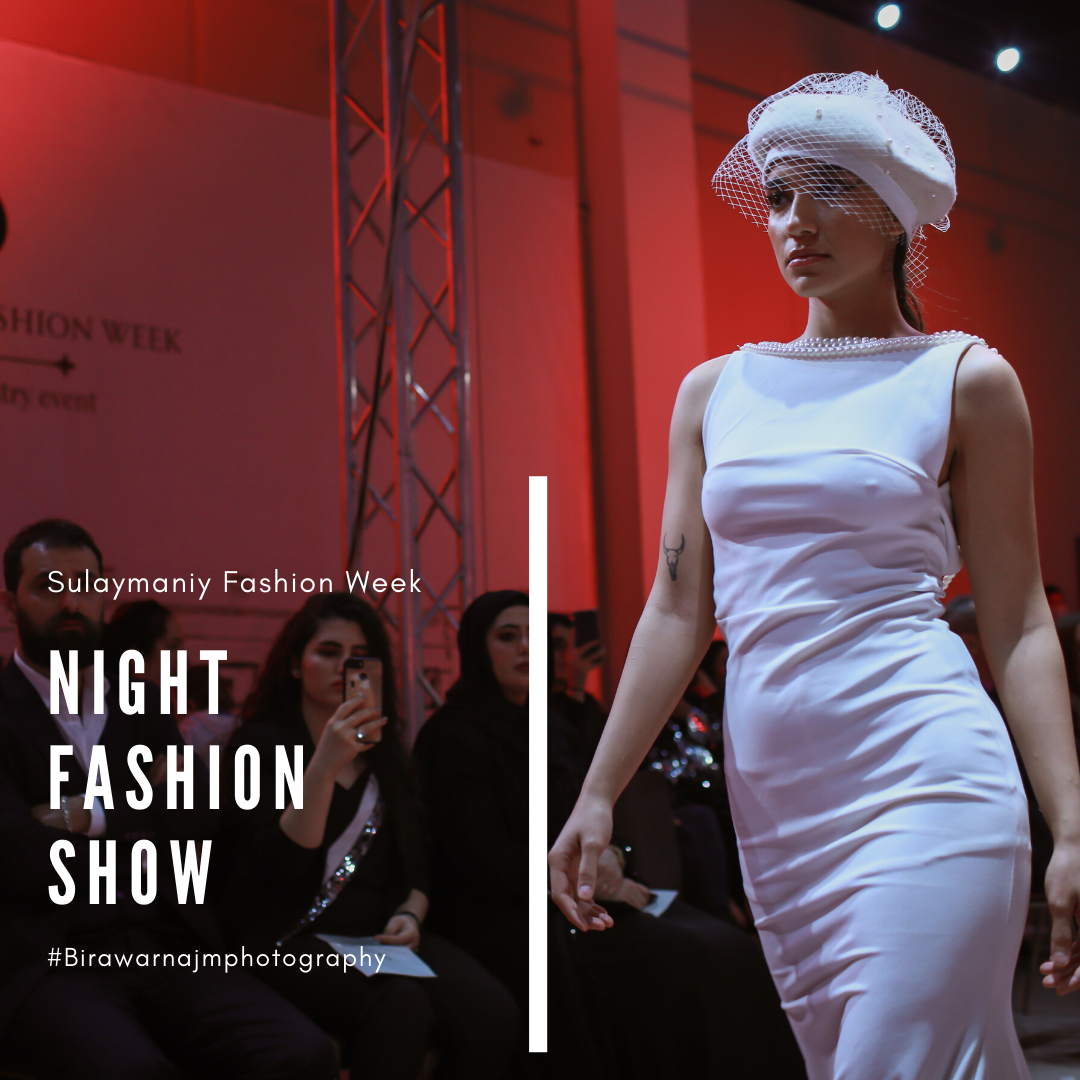 Model in sleek white dress and retro-style headpiece walks runway during Suleymaniy Fashion Week night show under red lighting.