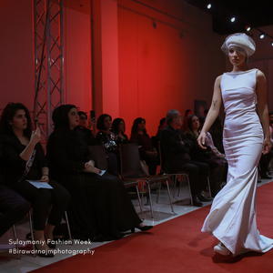 Model in white fitted gown walks down red carpet runway at Saigonese Fashion Week as audience watches.