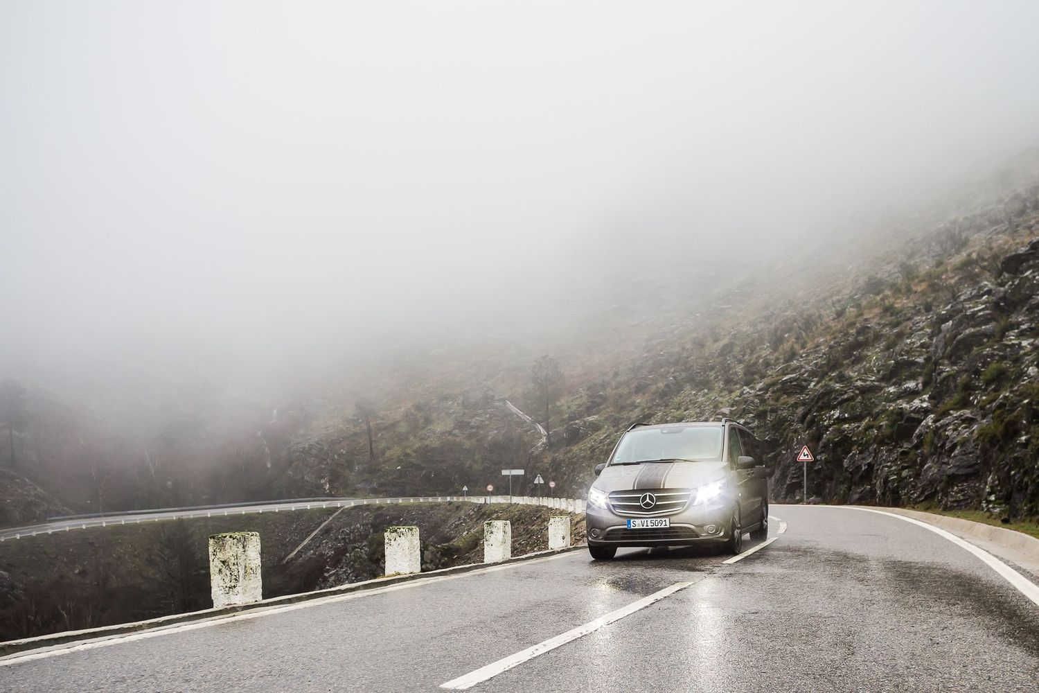 Car driving on a foggy mountain road with steep curves and guardrails.
