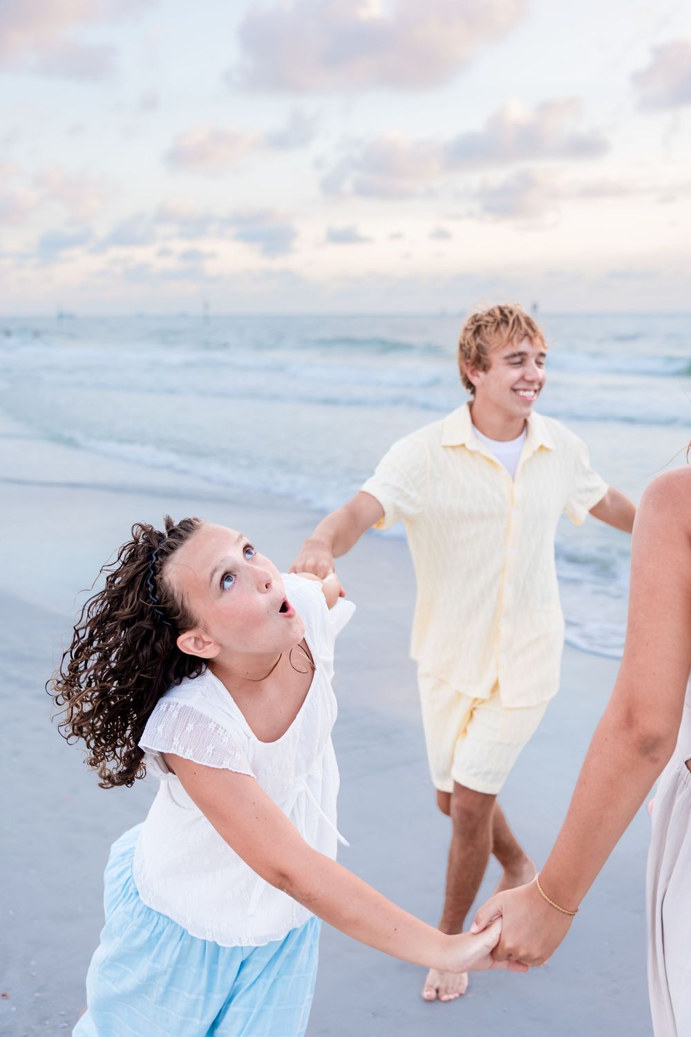 Family holding hands and playing on a sandy beach at sunset, smiling and having fun together.
