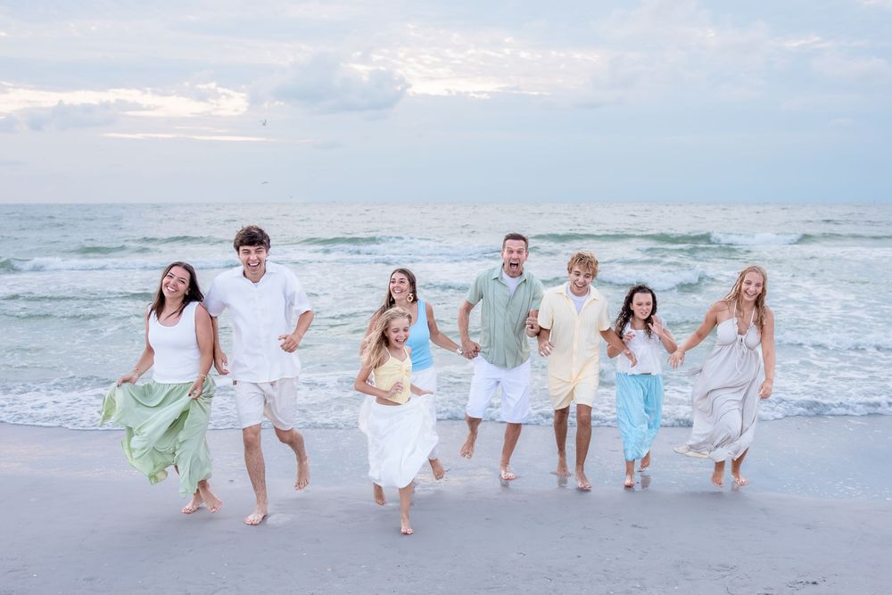 Happy family of eight running together on a sandy beach with ocean waves in the background.