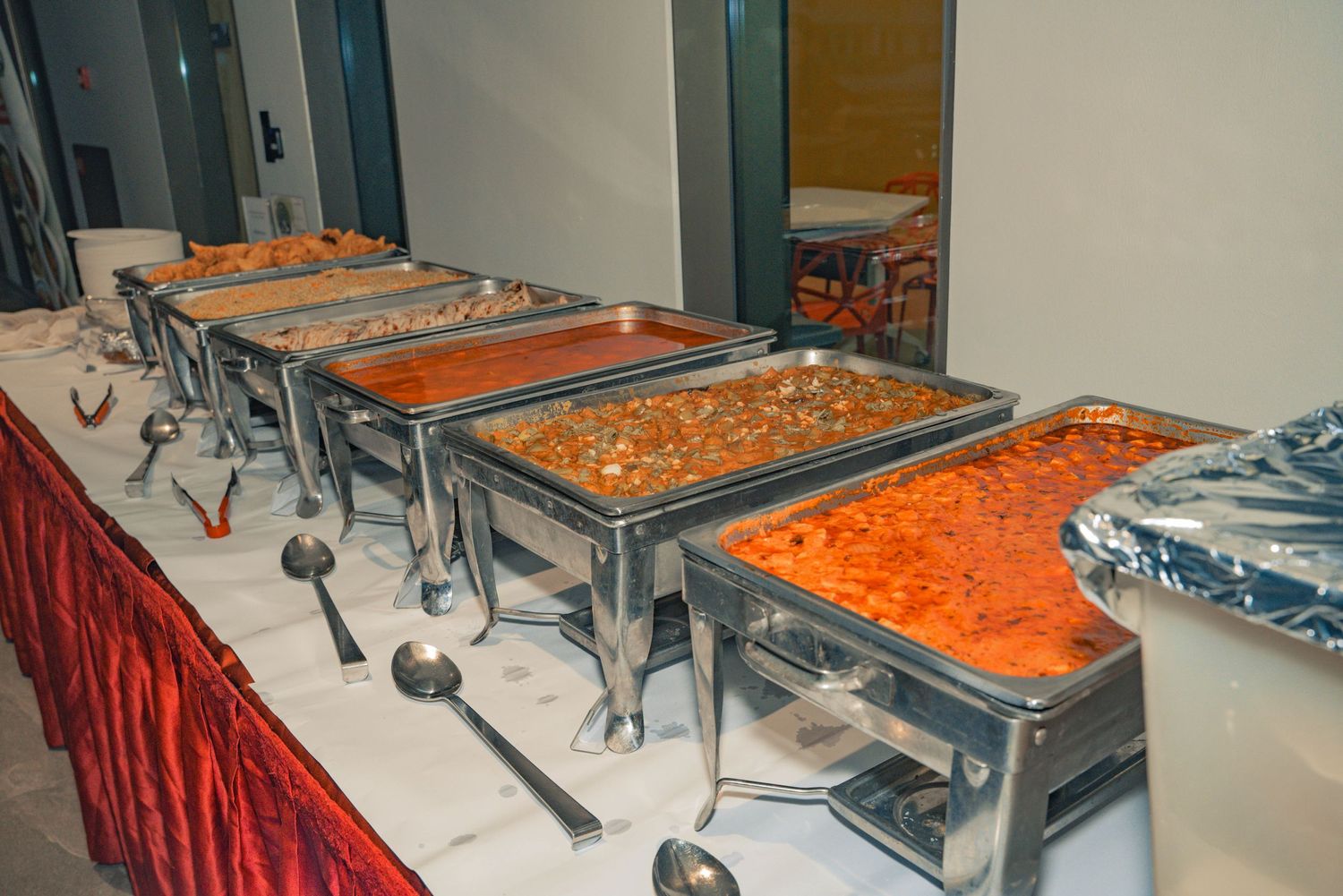 Buffet setup with stainless steel chafing dishes containing various Indian dishes.