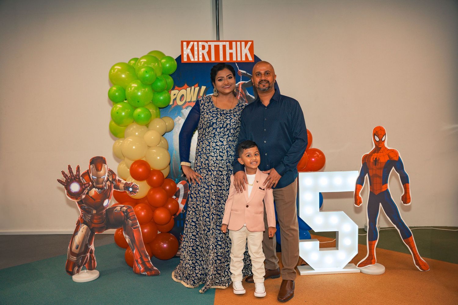Family poses at birthday celebration with Spider-Man standee and number 5 decoration.