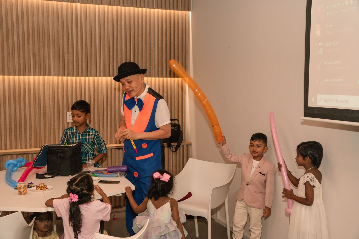 Children's entertainer performing with balloon art at indoor birthday party.