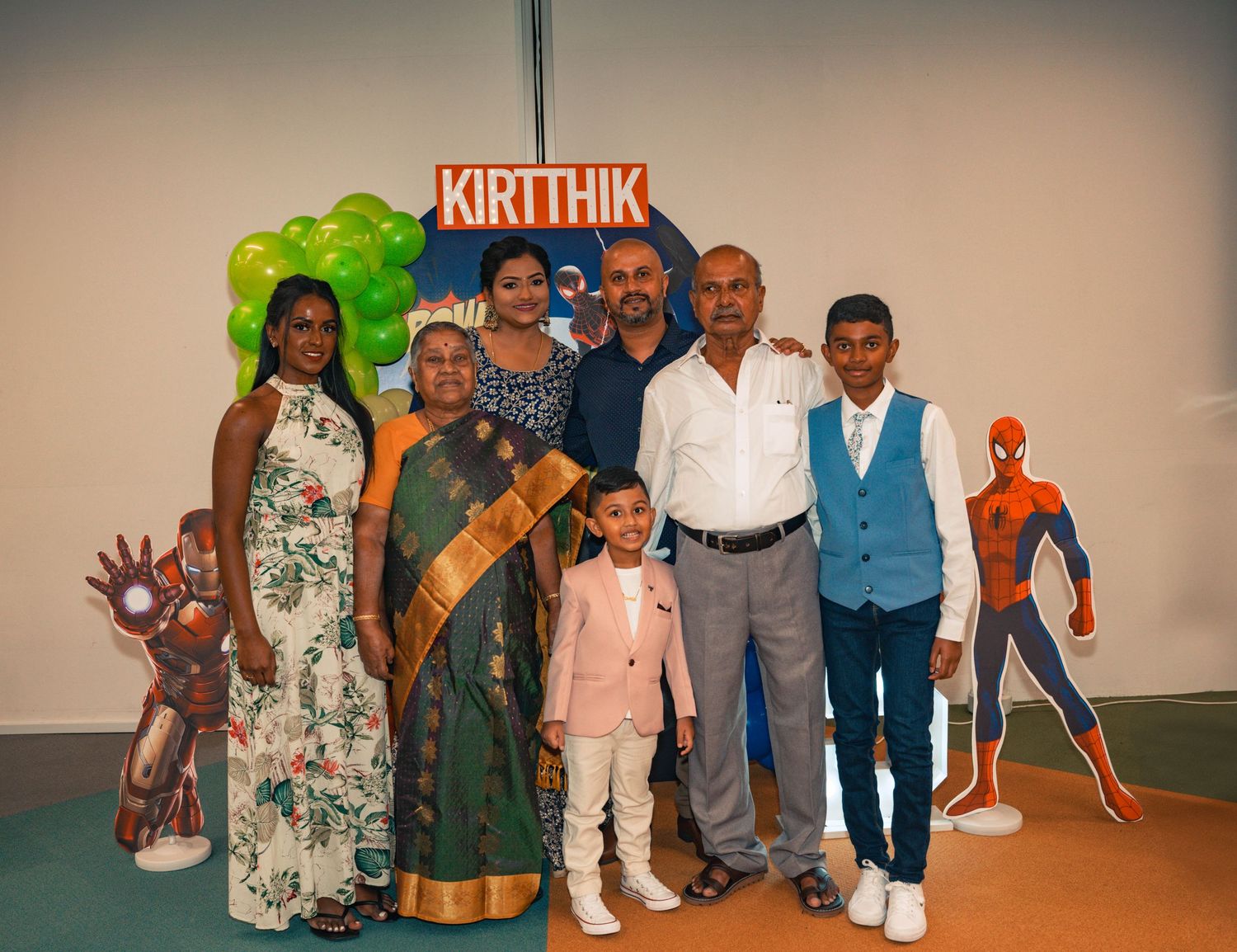 Family gathering at birthday party with superhero-themed decorations and balloon arrangements.