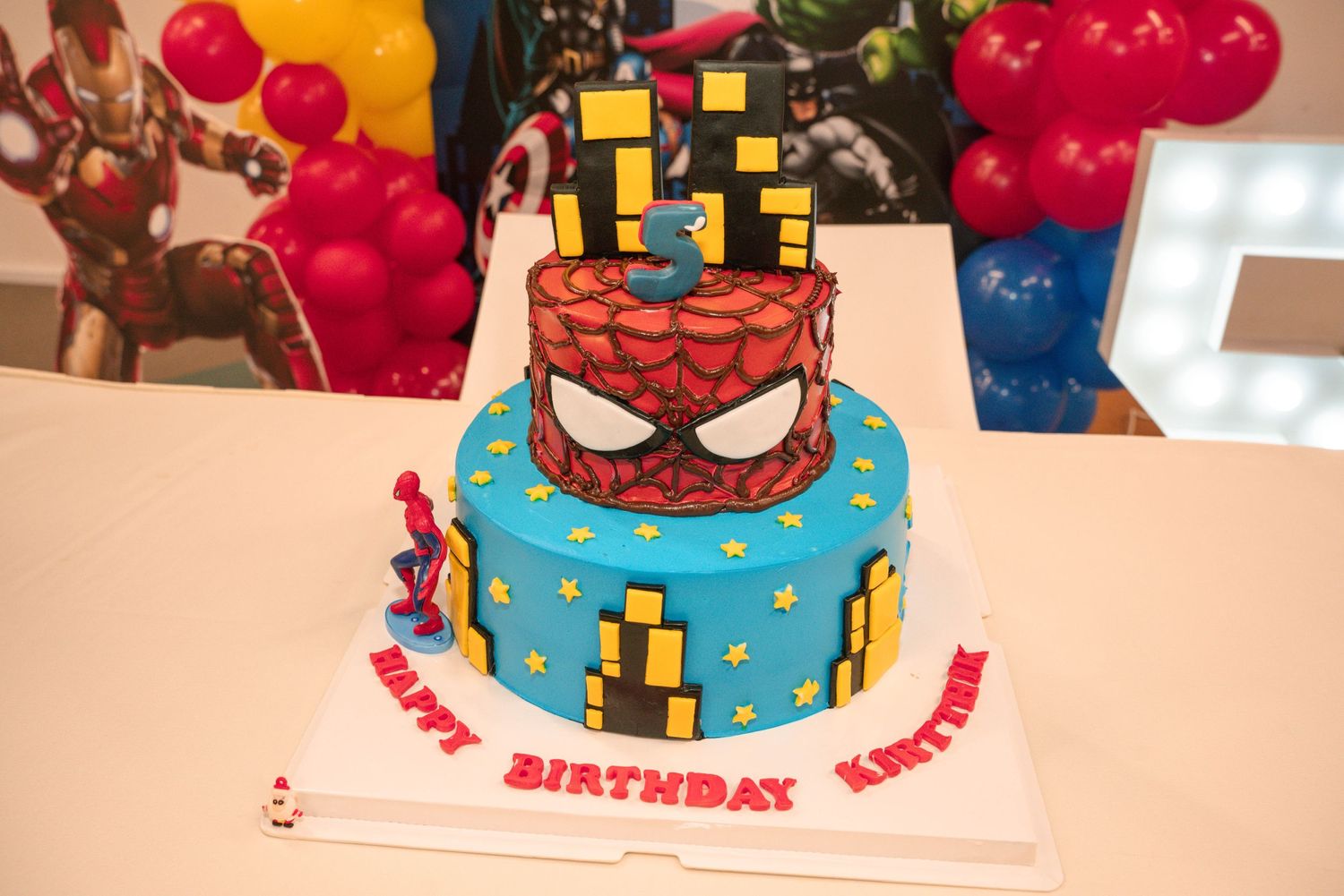 A Spider-Man themed birthday cake with blue frosting and city building decorations.