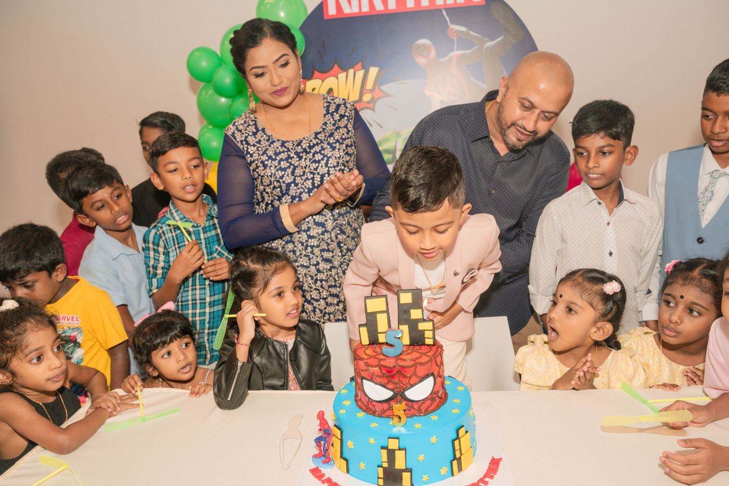Children gather around a Spider-Man themed birthday cake at a celebration party.