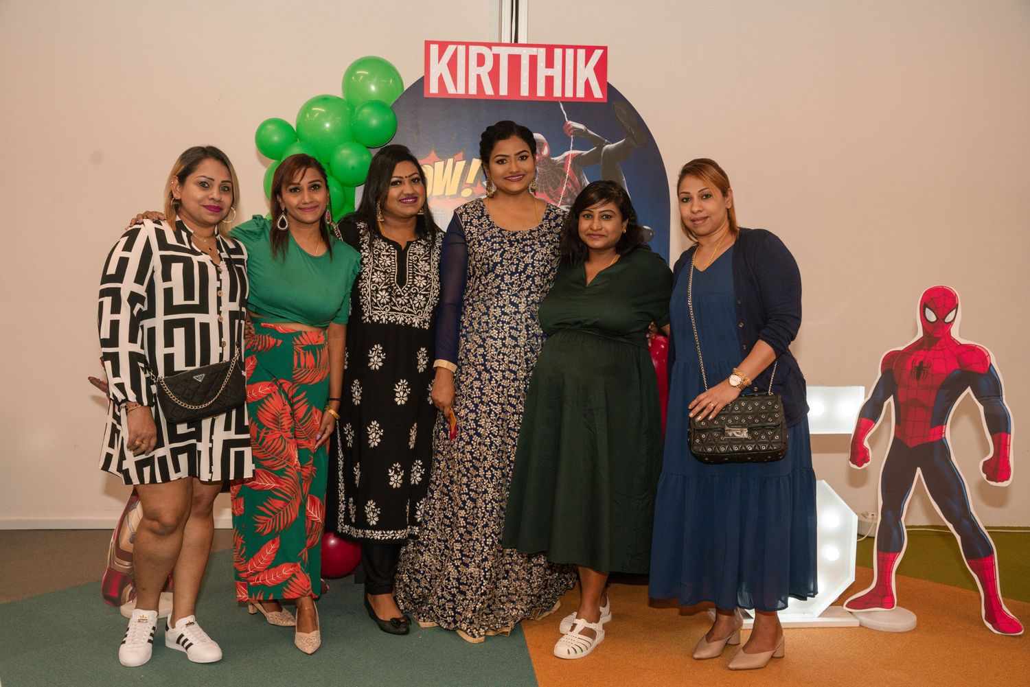 Group poses in front of superhero-themed birthday party backdrop with balloons and decorations.