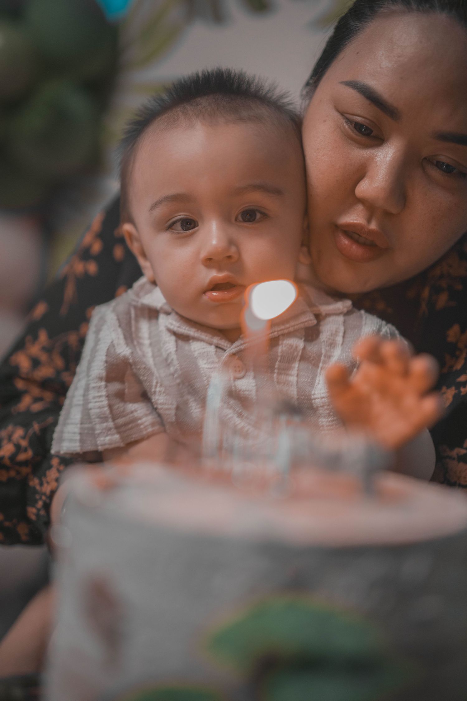 A young child in white clothing looks at birthday candles while being held.
