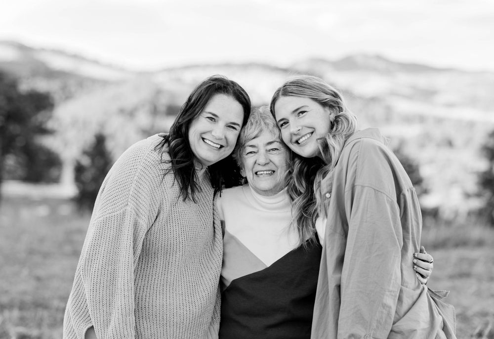 Black and white portrait of three people embracing and laughing together outdoors.