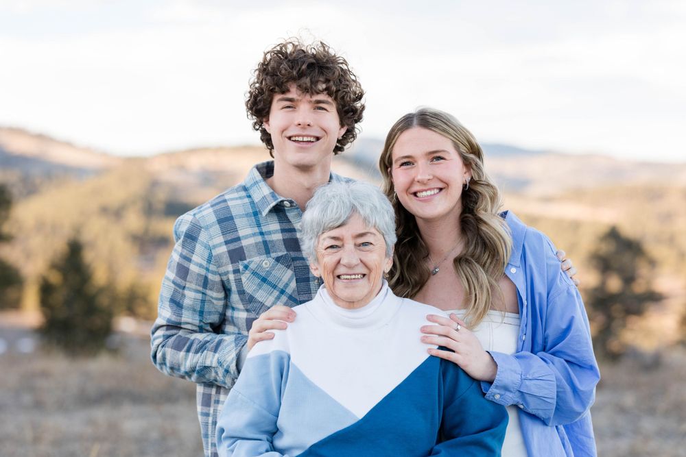 Three generations pose together against a mountainous landscape backdrop.