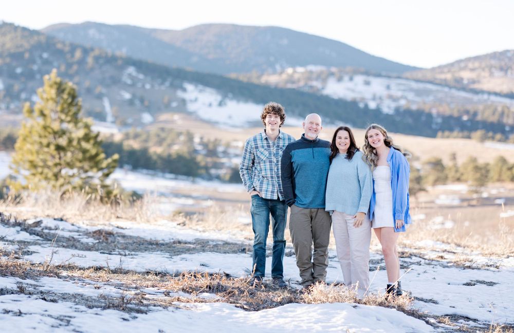 A group poses for a winter photo with a mountain backdrop and patches of snow on the ground.