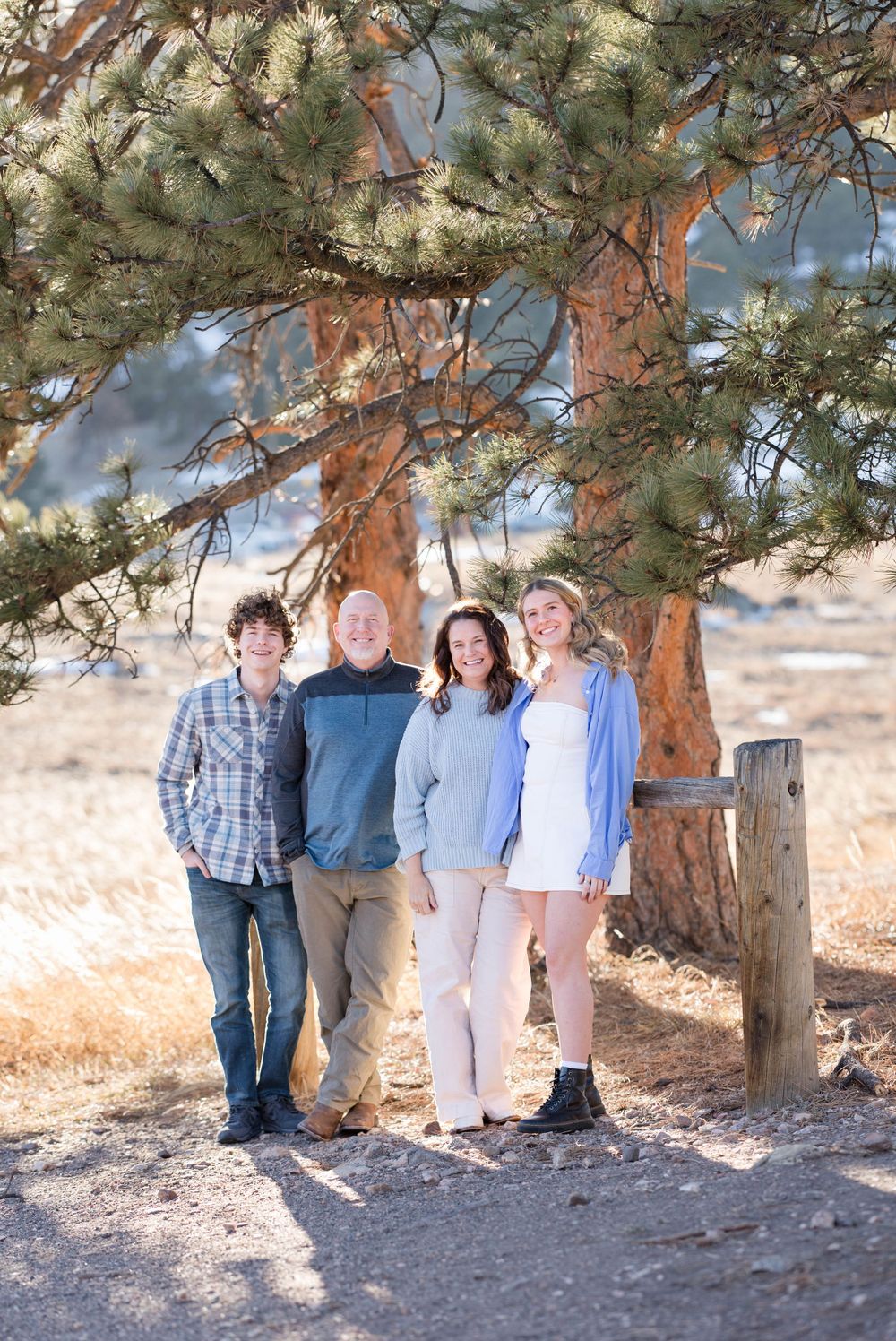 A group poses under a large pine tree on a mountain trail with golden afternoon light.