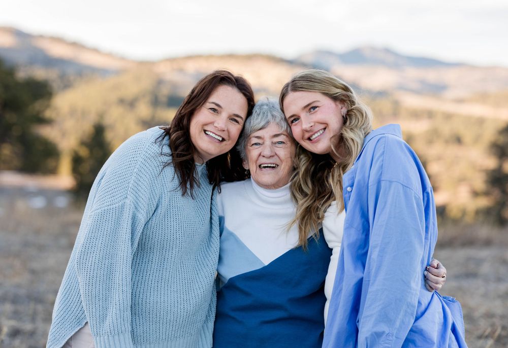 Three people share a joyful moment together outdoors with mountains in the background.