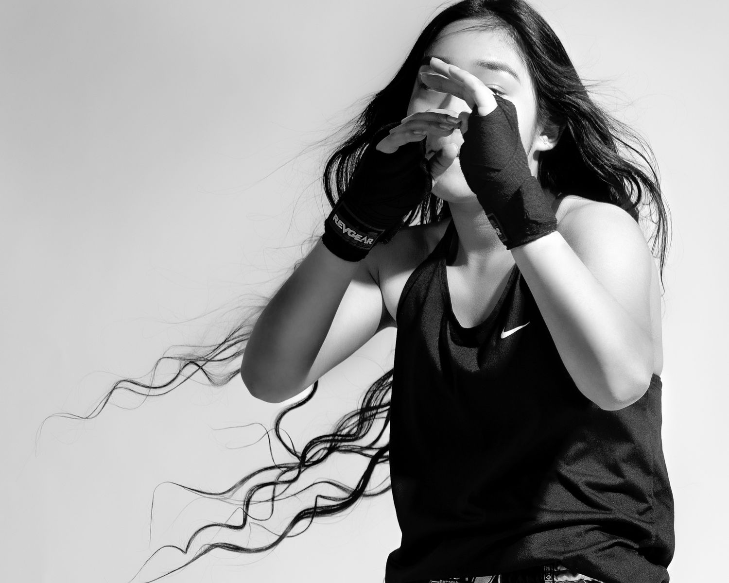 A black and white artistic portrait of someone taking a photograph with flowing dark hair in motion against white background.