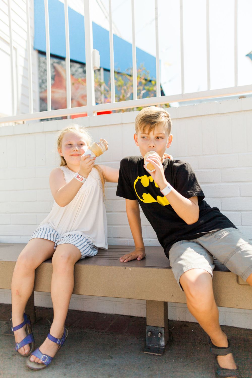 brother and sister eating ice cream on a bench, sister pretending to shove her ice cream cone on her brothers face