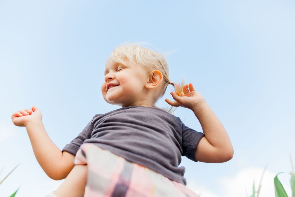 little girl closing her eyes being held up in the air, just sky behind her