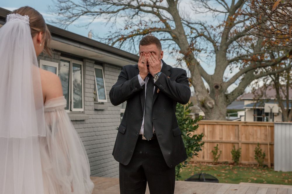 Emotional wedding moment captured on outdoor deck with white house and fence in background Cambridge New Zealand